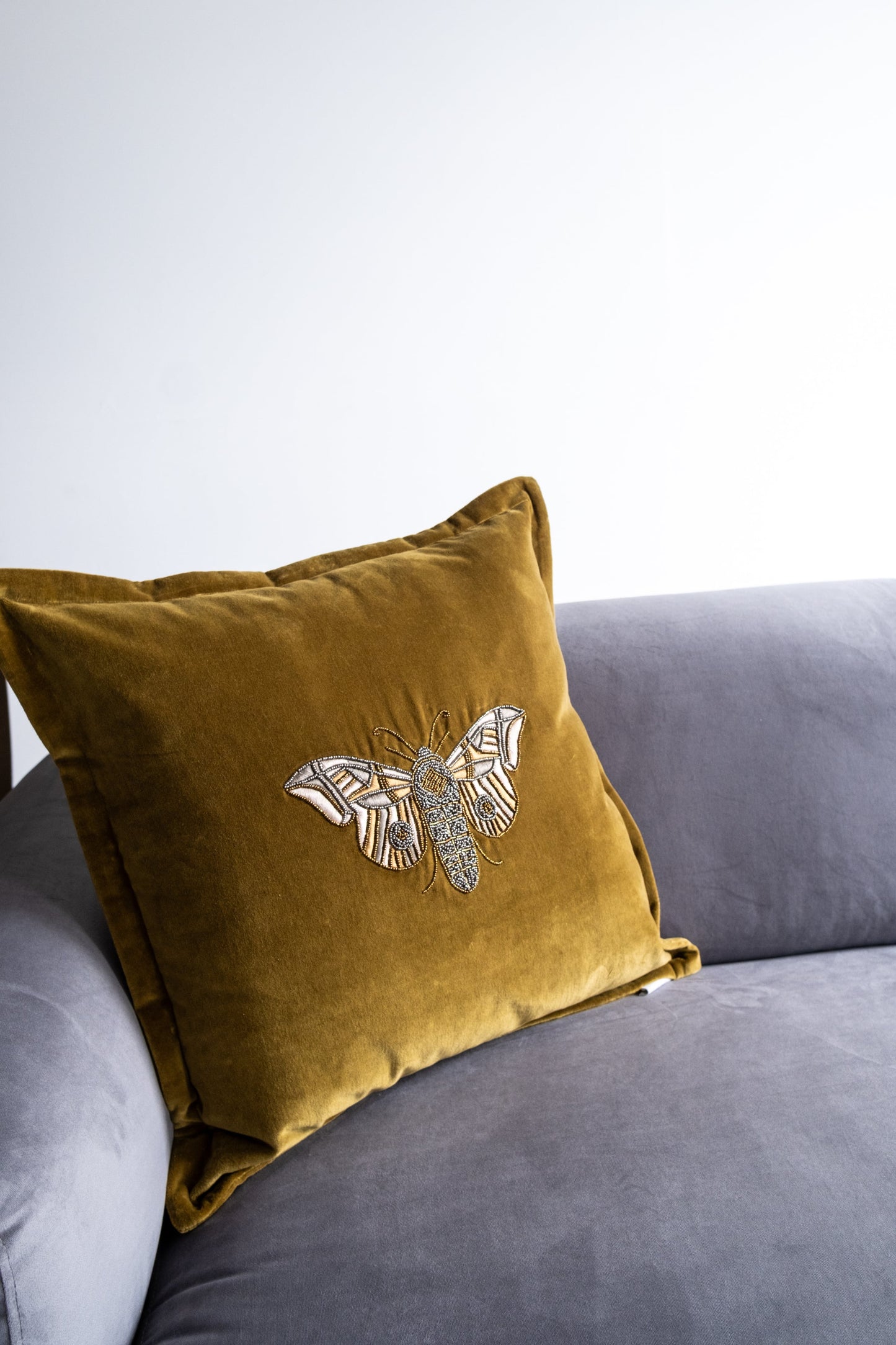 Gold pillow with butterfly design on a gray sofa against a white background
