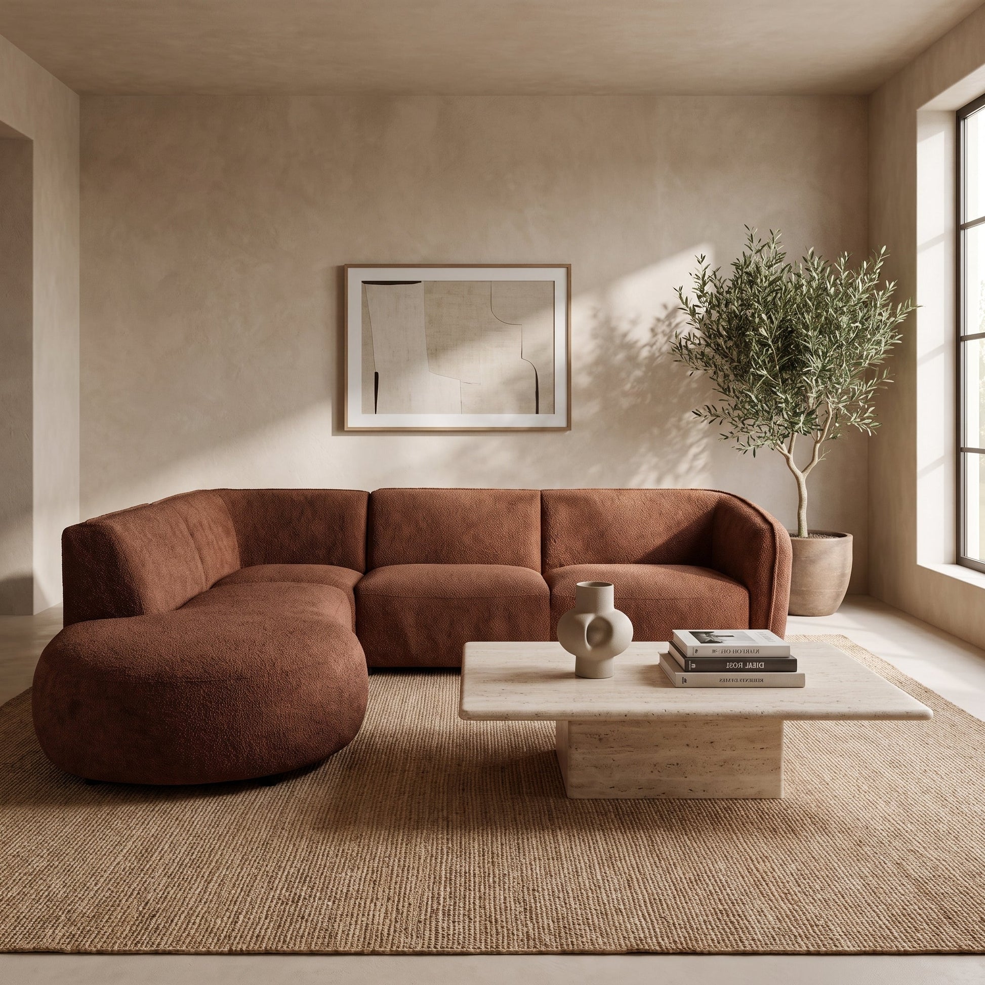A modern curved sectional sofa upholstered in a warm rust-brown fabric, styled in a minimalist living room with a light wood coffee table, textured rug, and a potted olive tree.