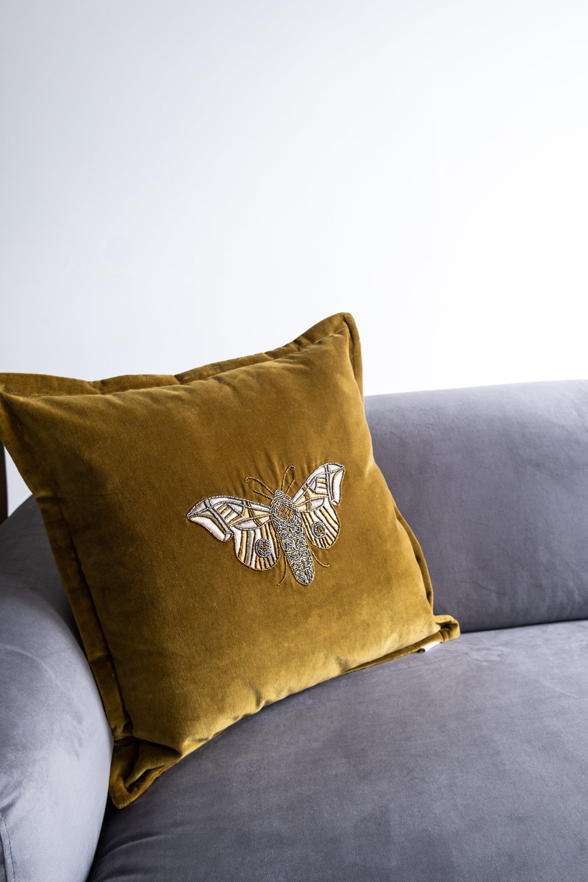 Gold pillow with butterfly design on a gray sofa against a white background