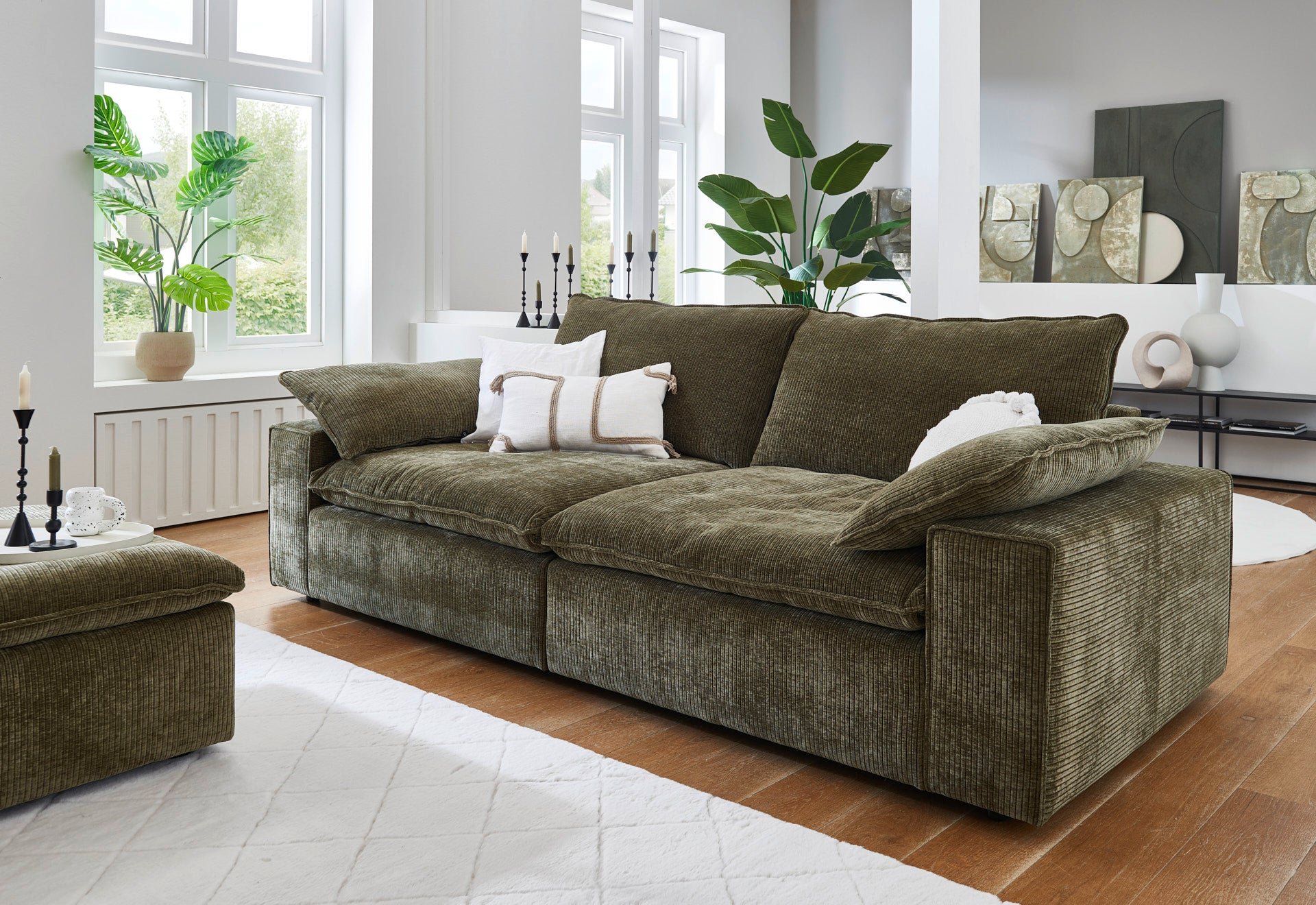 Green sofa in a living room with large windows and decorative items.