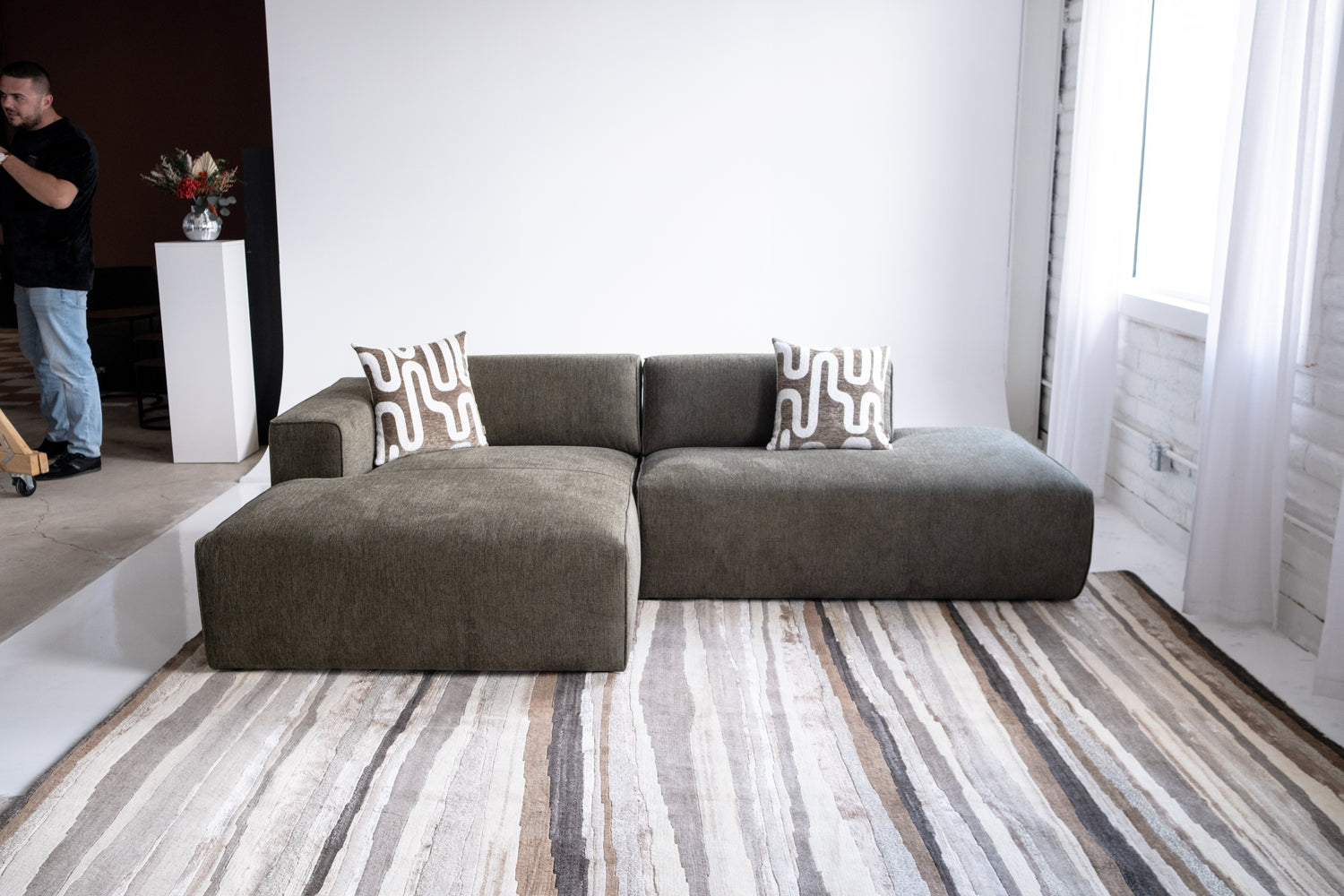 Green sectional sofa with patterned cushions on a striped rug in a room.