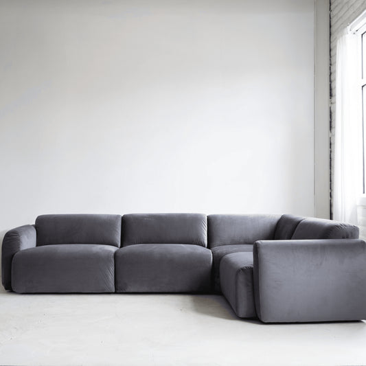 Gray sectional sofa in a minimalistic room with white walls and a window.