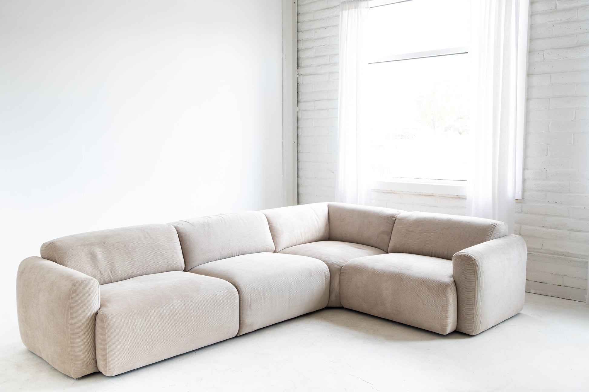 Beige sectional sofa in a minimalistic room with white walls and floor.