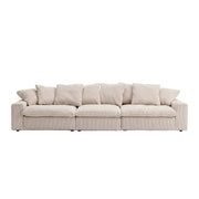 A modern three-seater sofa upholstered in a light beige ribbed fabric, featuring multiple square back cushions and matching throw pillows, set against a seamless white studio background.